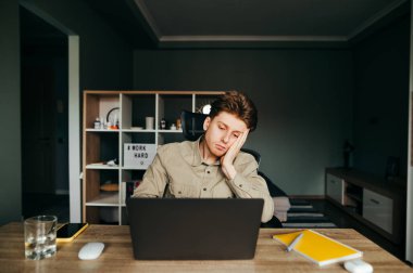 Masadaki yatak odasında oturan, dizüstü bilgisayar kullanan, ekrana bakan üzgün bir serbest yazar. Evdeki masada dizüstü bilgisayarla çalışan neşeli bir genç değil. Uzak çalışma.