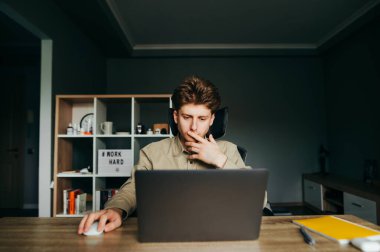 Samimi bir odada dizüstü bilgisayarla çalışan odaklanmış genç bir iş adamının portresi bir dizüstü bilgisayara odaklanmış. Freelancer evde çalışıyor. Uzaktan karantina çalışması.