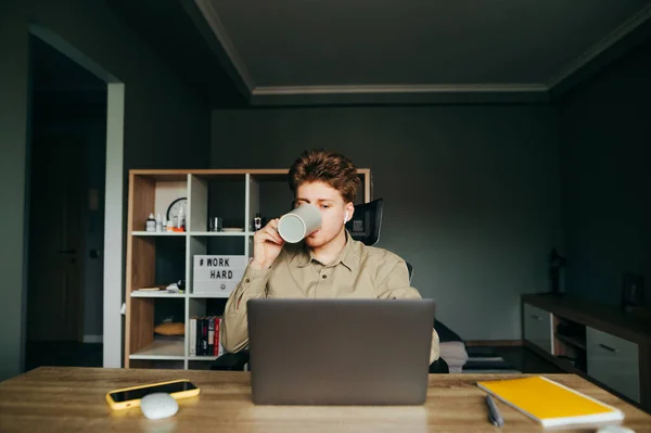 셔츠를 집에서 원격으로 컴퓨터를 컵에서 뜨거운 음료를 마시는 노동자 헤드폰을 — 스톡 사진