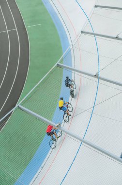 Üç bisikletçi Velodrome 'da turluyor, yarış pistinde bisiklet sürüyor. Üst Manzara. Geçmişi. Dikey. Bisikletçiler açık havada bisiklet sürerler. Yarışmadan önce antrenman