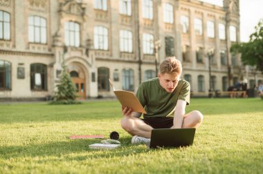 Konsantre olmuş genç adam, bir üniversite binasının arka bahçesinde çimlere oturur ve elinde dizüstü bilgisayarla ders çalışır. Kampüs çimenlerinde öğrenci mola için hazırlanır ve bir derse hazırlanır.