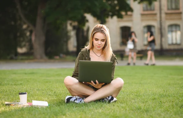 迷人的两岁随和学生坐在大学公园的草坪上 一边看书 一边喝咖啡 用笔记本电脑 一位漂亮的女士坐在校园的草地上 一边用笔记本电脑上网 — 图库照片