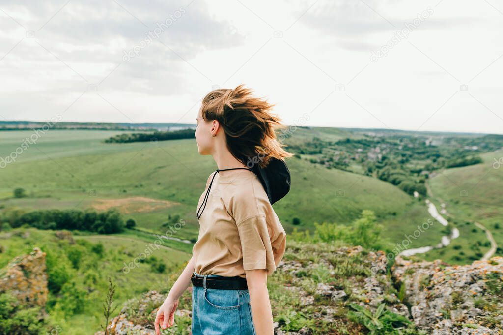 Hipster girl is standing on a rock in the background of a beautiful Ukrainian landscape and enjoys the view. Woman tourist traveling in Ukraine.