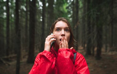 Genç bayan turist dağ ormanında korkmuş ve şok olmuş hissediyor, telefonla konuşuyor, eliyle ağzını kapatıyor. Ormanda kaybolmuş bir kız gezgin. Korkuyor, telefonla arıyor..