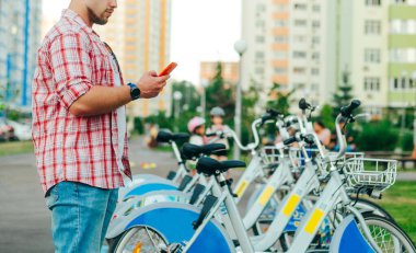 Günlük kıyafetler giyen bir adam bisikletin yanında durur ve akıllı telefondan bir uygulama aracılığıyla bisiklet kiralar. Sakallı bir adam akıllı telefonunda bisiklet paylaşmaktan hoşlanır. Bisiklet kiralama