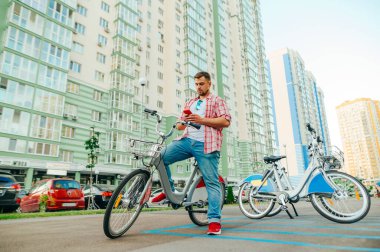 Gömlekli ve sakallı yetişkin bir adam parlayan bir bisiklete biner ve akıllı telefon kullanır. Turist mobil bir uygulama aracılığıyla bir bisiklet kiralıyor. Eko taşımacılığı