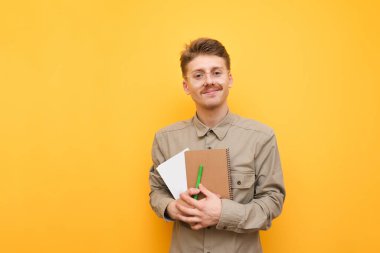 Gömlek ve gözlük takmış yakışıklı bir erkek öğrencinin portresi sarı arka planda elinde kitaplarla ve egzersiz kitaplarıyla kameraya bakıyor ve gülümsüyor. Gözlüklü ve bıyıklı güzel bir inek.