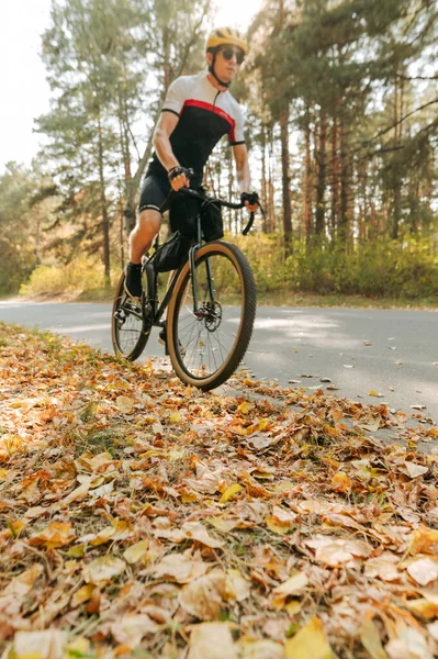 Man rides a bicycle on a fallen yellow leaf. Bicycle walk through the autumn forest. Focus on the leaves under the wheels of the cyclist. Vertical.