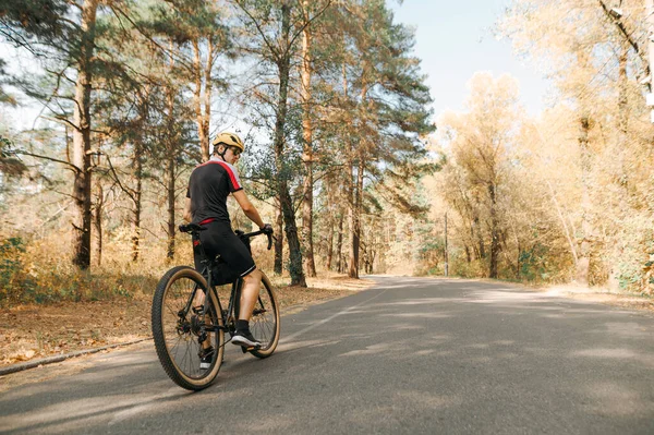 在秋天的森林里骑自行车站在路上休息 戴着头盔和运动服的职业骑手在森林路上行走 复制空间 — 图库照片
