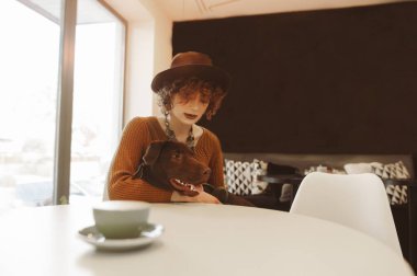 Şapkalı ve kazaklı hippi kız rahat bir kafede köpekle oturuyor. Kahve dükkanında köpek ve bir fincan kahveyle rahatlayan bir kadın. Hayvan dostu kafe..
