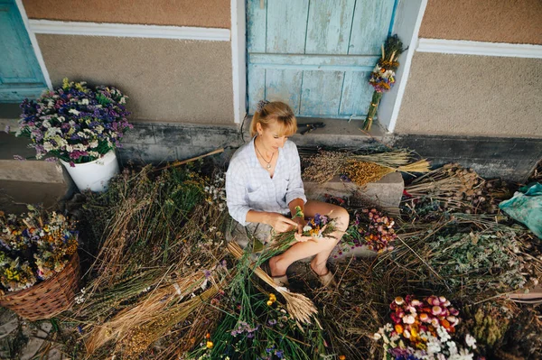 Woman sitting in dried flowers outside the city and beautiful holiday bouquets. Amateur florist makes a festive arrangement of dried flowers.
