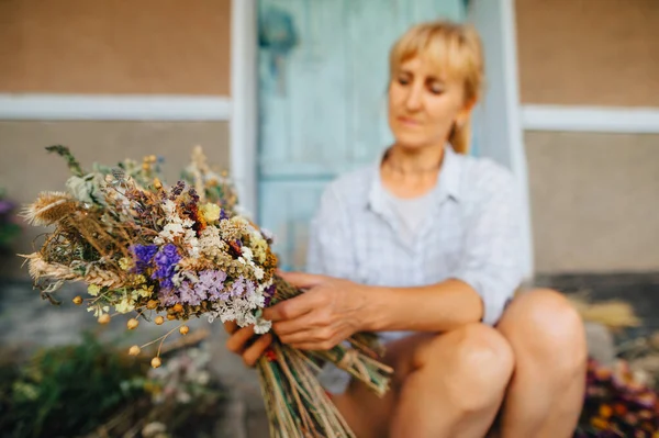 Bouquet of dried flowers in the hands of an adult woman creates a composition. The florist makes a composition of dried flowers grown in the garden in the country.
