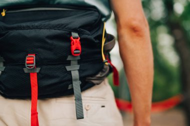 Yakın plan, kırpılmış fotoğraf. Ormanda arka planda bulanık bir geçmişi olan bir adamın kemerinde seyahat etmek için bel çantası.