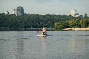 Kaslı atletik genç adam yazın boş zamanlarını nehirde geçiriyor, kürek çekiyor. Güneşli bir günde yemek tahtasında çalışmak.