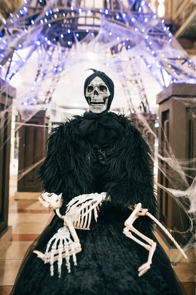 Skeleton of a woman with the bones of an animal in her arms indoors on a background of lights. Halloween decorations. Vertical.
