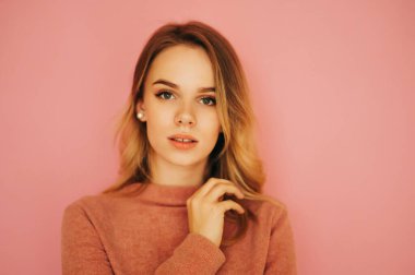 Pembe kazaklı çekici kadın pembe arka planda duruyor ve kameraya seksi bir yüzle poz veriyor. Boşluğu kopyala.