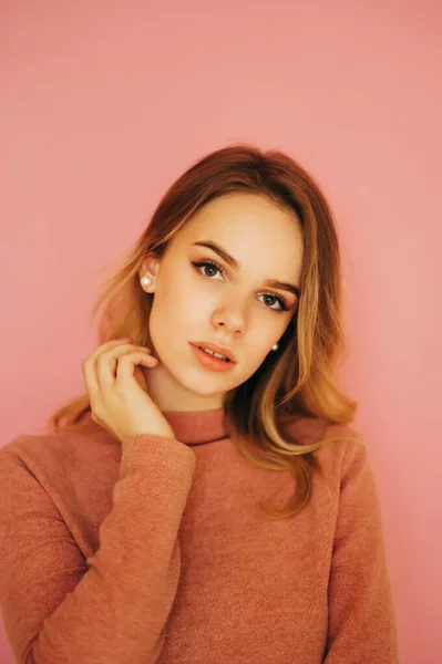 Vertical portrait of attractive woman in sweater posing at camera with seductive face on pink background. Isolated.