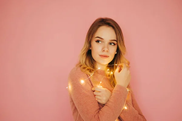 真面目な顔をしたコピースペースを脇に見て 手にクリスマスライトでピンクの背景に隔離されたかわいい若い女性 お正月とクリスマス — ストック写真