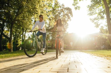 Genç bir çift, sonbahar sezonunda gün batımının arka planında parkta bisiklet sürüyor. Hafta sonu bir arkadaşla bisiklete binmek..
