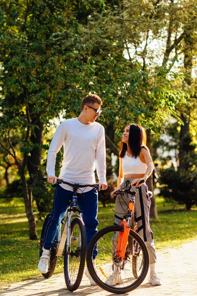快乐的女人和男人骑自行车站在秋天的公园里 满脸笑容地聊天 可爱的一对夫妇时髦的年轻人骑自行车 垂直方向 — 图库照片