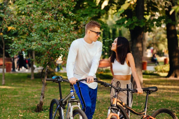 秋の公園に自転車で立っている若い夫婦を愛し 彼らの顔に笑顔で話してください 秋の自転車レジャー — ストック写真