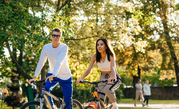 秋の公園で自転車に乗るスタイリッシュな美しいカップル 秋の都会の公園を自転車で歩く若者たち — ストック写真