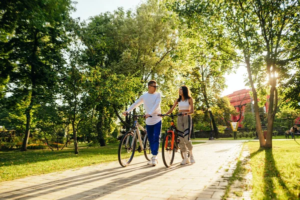 一对年轻漂亮的夫妇骑着自行车在公园的小巷里交流 秋天的时候 男人和女人骑着自行车穿过公园 聊着天 — 图库照片