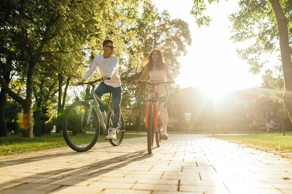 在日落的背景下 一对年轻夫妇在公园里骑自行车 周末和朋友一起骑车 — 图库照片