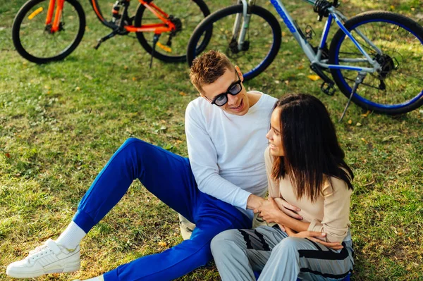 一对快乐的年轻人在公园的草地上骑自行车玩乐 一个男人和一个女人在公园里散步 坐在草坪上放松一下 玩得很开心 — 图库照片
