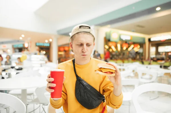 Zabawny Młody Człowiek Stoi Hamburgerem Szklanką Coli Ręku Wygląda Zdenerwowanego — Zdjęcie stockowe