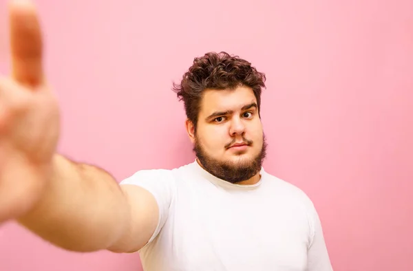真剣に髭を生やした太りすぎの男がピンクの背景に立って自撮り カリスマ的な太った男は 真剣な顔をしたカメラを見て ピンクの背景で写真を撮ります — ストック写真