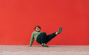 Kırmızı bir duvarın arkasında hip hop dansı yapan şişman bir genç. Tostun kırmızı arka planda dans topu performansı gösteriyor.