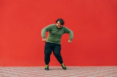 Kırmızı duvarda dans eden, sıradan giysili, karizmatik, pozitif şişman bir adam. Şişman bir adam sokakta dans gösterisi yapıyor..
