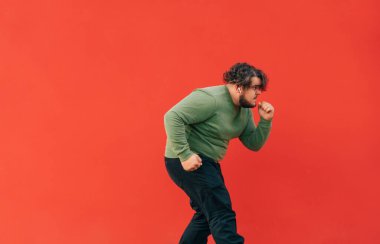 Şişman ve yeşil tişörtlü komik kıvırcık adam kulaklıkla müzik dinliyor ve kırmızı arka planda dans gösterisi yapıyor. İzole edilmiş.