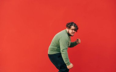 Etkileyici kıvırcık şişko adam kulaklıkla müzik dinliyor ve kırmızı arka planda dans ediyor..