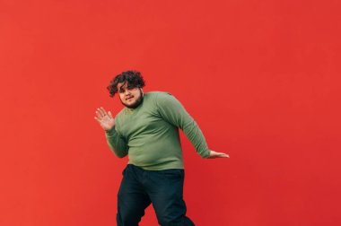 Kıvırcık saçlı, kilolu, kırmızı arka planda hip hop yapan karizmatik bir genç. Şişman adam izole bir dans gösterisi sergiliyor..