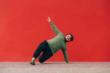 Pozitif kilolu genç adam kırmızı duvarın arkasında dans gösterisi sergiliyor, kameraya bakıyor ve gülümsüyor..