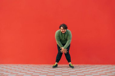 Kıvırcık saçlı komik şişman adam kırmızı duvarda dans ediyor ve gülümseyerek kameraya bakıyor. Kırmızı arka planda dans eden kilolu adam..