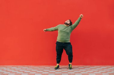 Kırmızı duvarda dans eden, sıradan giysili, şişman, karizmatik genç bir adam. Kırmızı arka planda dans eden şişman adam..