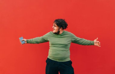 Kıvırcık saçlı, kırmızı arka planda dans eden, elinde kulaklığı kulaklığı olan komik şişman bir adam. İzole edilmiş.