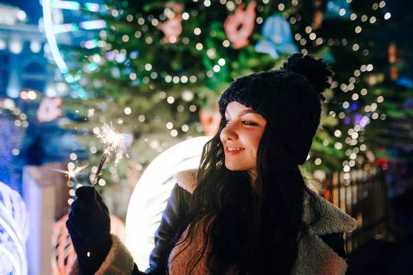 暖かい服の女性のクローズアップクリスマスの肖像画は 通りのクリスマスツリーの背景に輝く人を照らします 離れて見て クリスマスストリートで時間を過ごします — ストック写真