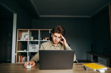 Düşünceli bir müteahhidin portresi rahat bir odada oturuyor ve ciddi bir yüzü olan bir dizüstü bilgisayar üzerinde çalışıyor, ekrana odaklanıyor. Düşünceli bir çalışan evden uzakta çalışıyor..