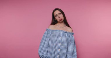 Bir kadın canlı pembe bir arka plana karşı özgüvenle duruyor. Mavi, kareli, omuzsuz bir bluz giyiyor ve düşünceli bir ifade sergiliyor. Ayarlara neşeli bir hava katıyor..