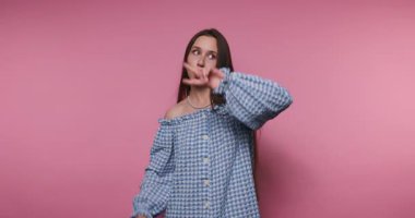 Neşeli genç bir kadın hayat dolu kişiliğini barış işaretleri yaparak ve sıcak bir şekilde gülümseyerek paylaşıyor. Pembe arka plan neşeli atmosfere katılır, pozitiflikle dolu neşeli bir anı yakalar..