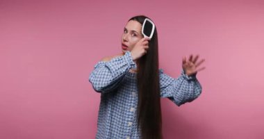 Genç kız, saç bakım rutinini parlak pembe bir zemine karşı fırçalayarak sergiliyor. Sağlıklı saç bakımını ve saç bakım tavsiyelerini ilgi çekici bir şekilde vurguluyor..