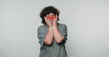 Bireyler düz bir zemine karşı duruyor, yüzlerini ellerle örtüyorlar. Minimalist bir alanda bir anlık yansıma ya da duyguyu somutlaştıran bir meyve parçası tutarlar..