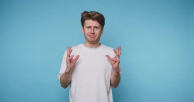 Genç bir adam saf mavi bir altyapının önünde duruyor, belli bir konudaki düşüncelerini paylaşırken tutkuyla işaret ediyor. Anlamlı hareketleri güçlü duyguların göstergesi..