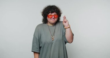 Ateşli genç bir kadın, şans dilemek için kapalı bir alanda şans diliyor. Turuncu güneş gözlüğü ve gevşek gri bir bluz giyiyor..