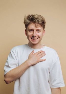 Genç adamın portresi elini göğsüne koyduğunda sıcak bir şekilde gülümsüyor, bej arka planda samimiyet ve dostluk taşıyor.