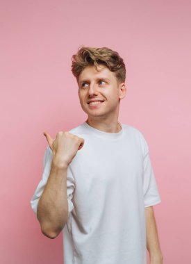 Genç, neşeli bir adamın portresi gülümserken başparmağını kaldırıyor, pembe arka planda pozitiflik ve cesaret veriyor.